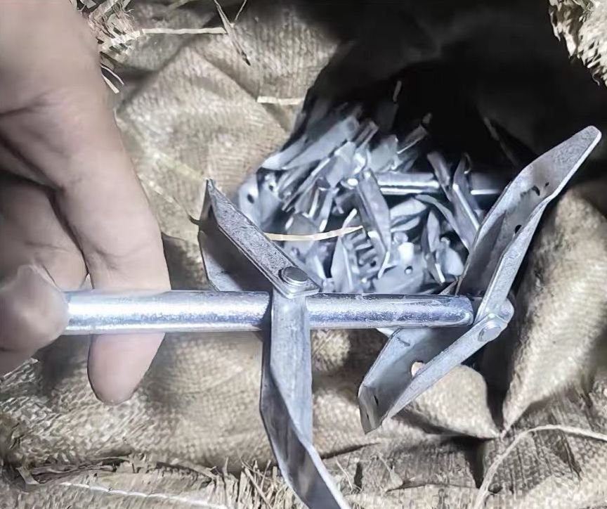Close-up of folding duckbill earth anchor hinge and folded blade profile, showing simple stamped-steel construction.